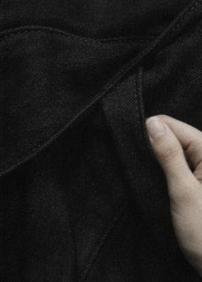 Close-up of a person's hand touching black denim fabric, possibly jeans.