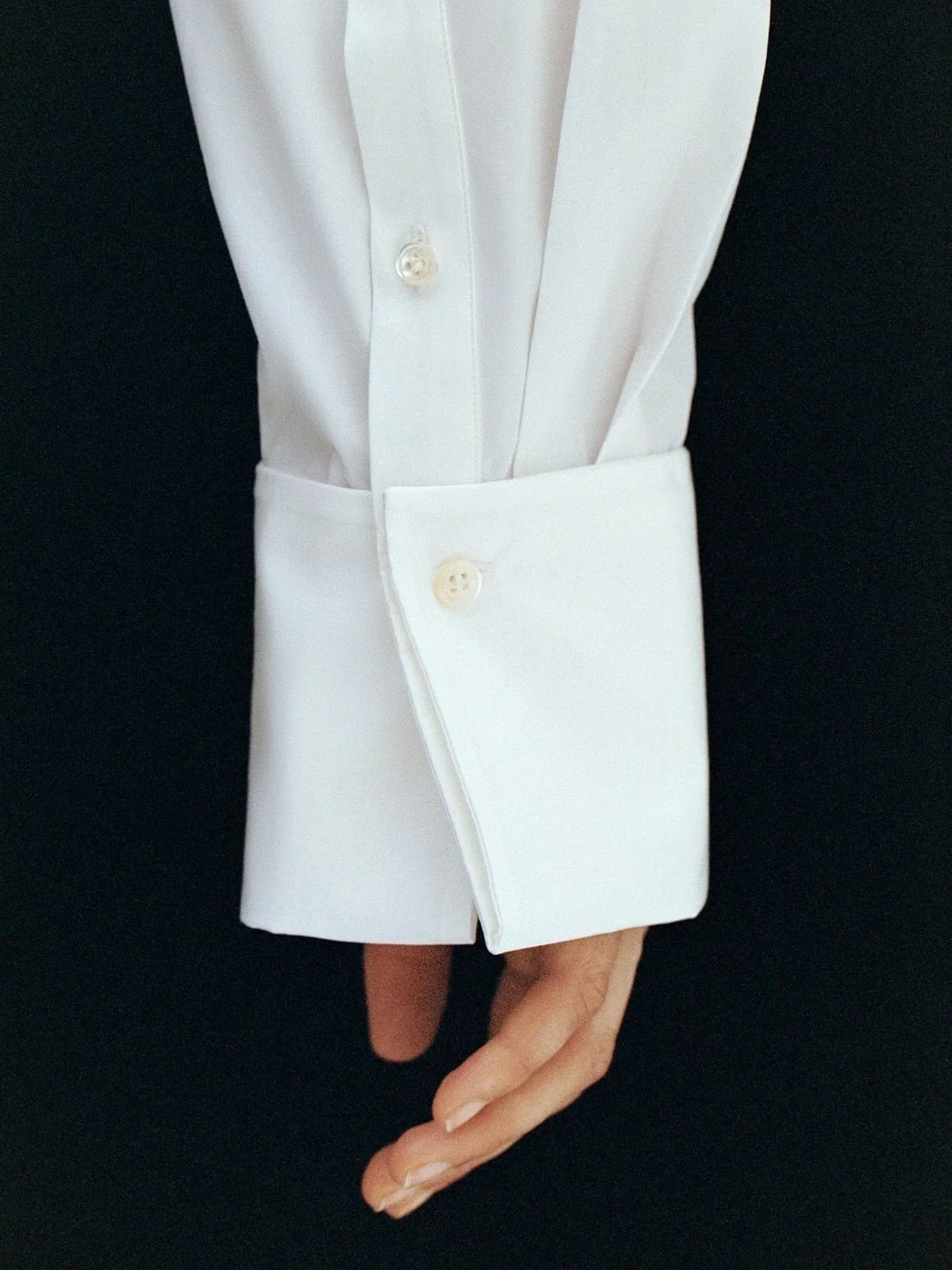 Close-up of a person wearing a white dress shirt with French cuffs, turned back and fastened with a cufflink, against a black background.