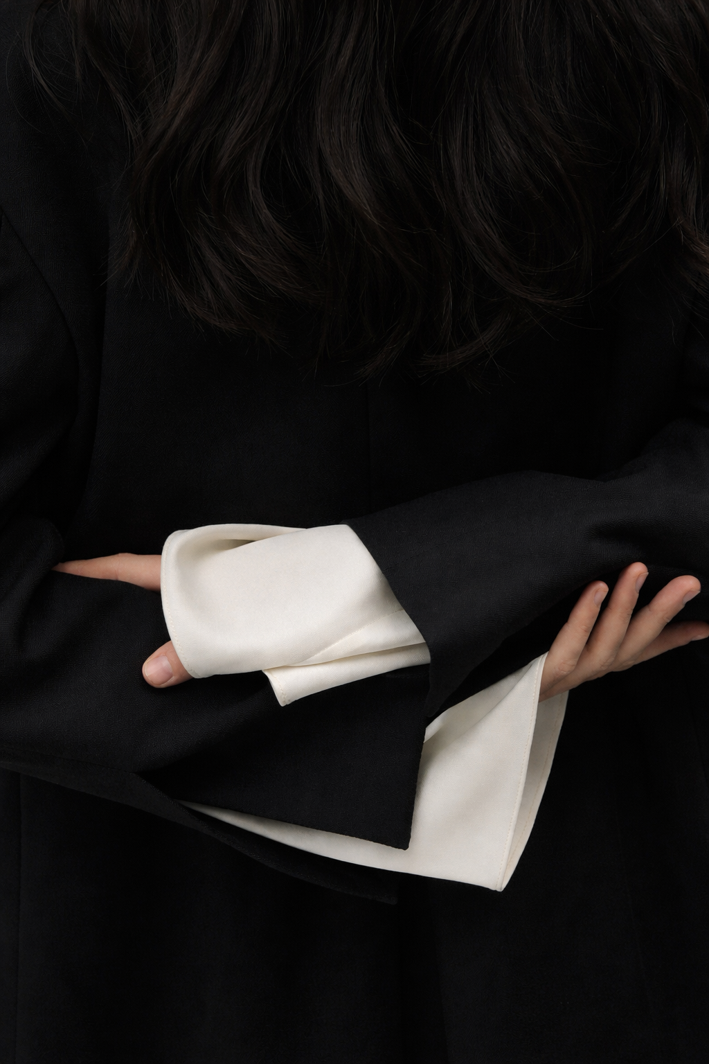 Close-up of a person wearing a black blazer with rolled-up white shirt cuffs, arms crossed.