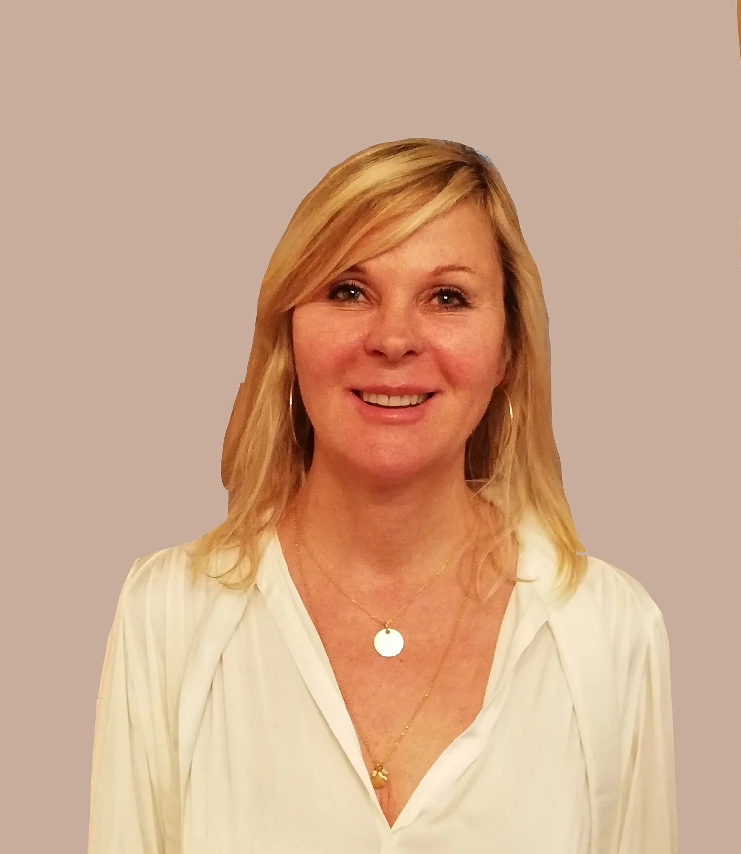 Portrait d'une femme blonde souriante portant une chemise blanche et des colliers, avec un fond beige.