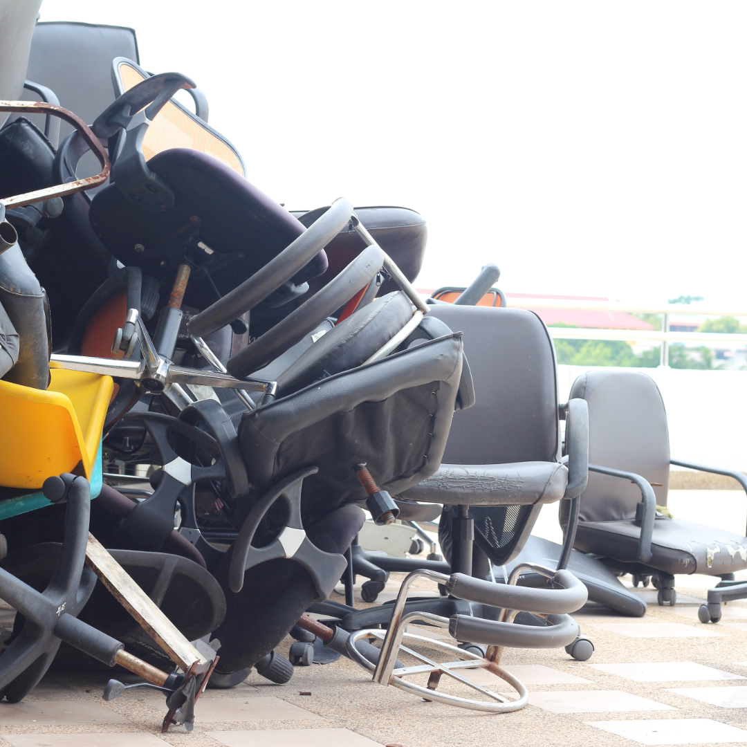 Pile of discarded office chairs and miscellaneous items outdoors.
