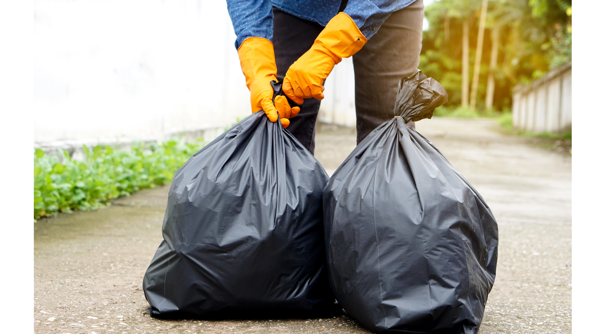 Person wearing orange gloves picking up trash and holding two large black garbage bags