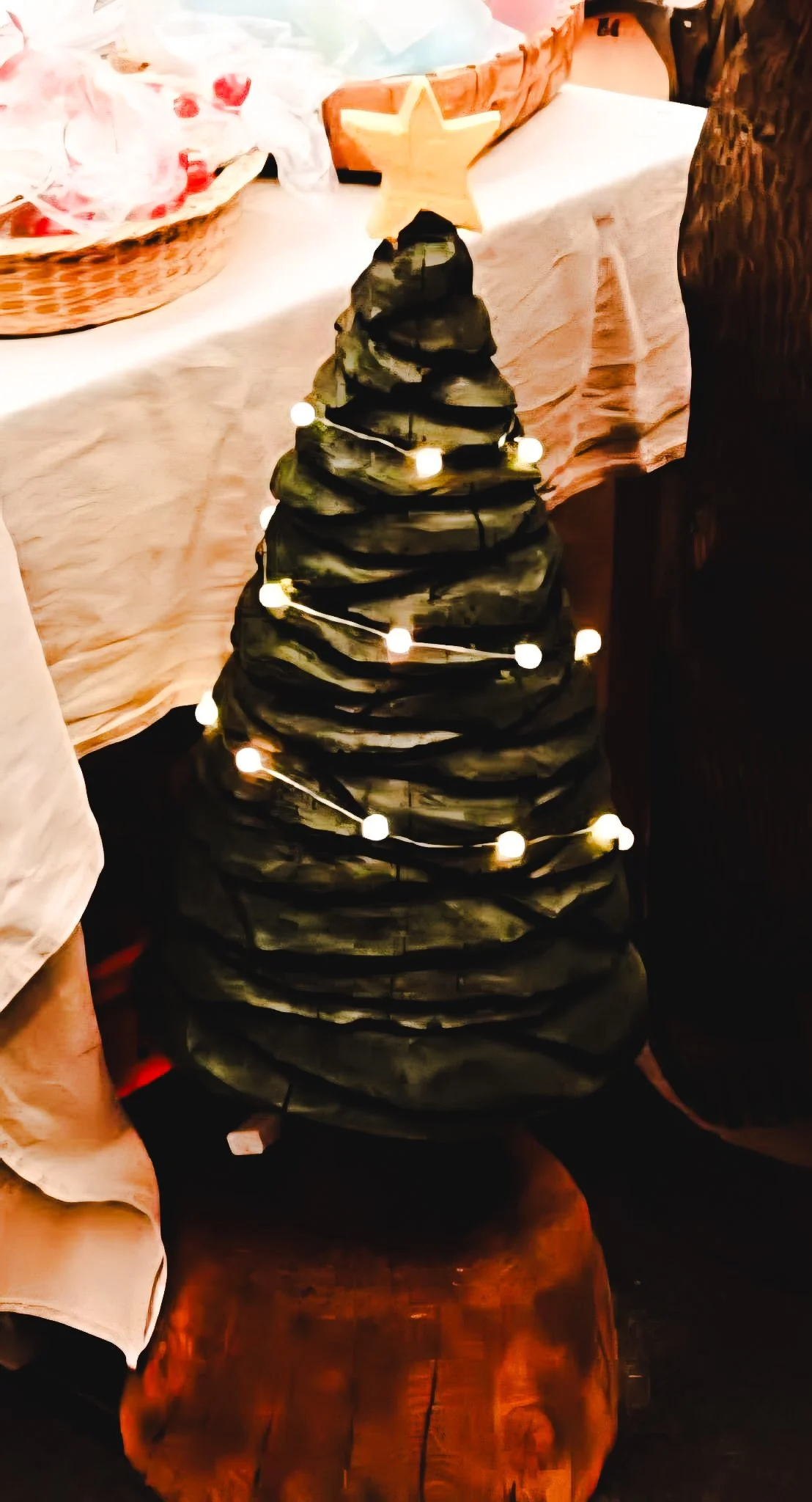 A small Christmas tree made of layered stones, decorated with a string of warm white fairy lights and topped with a wooden star.