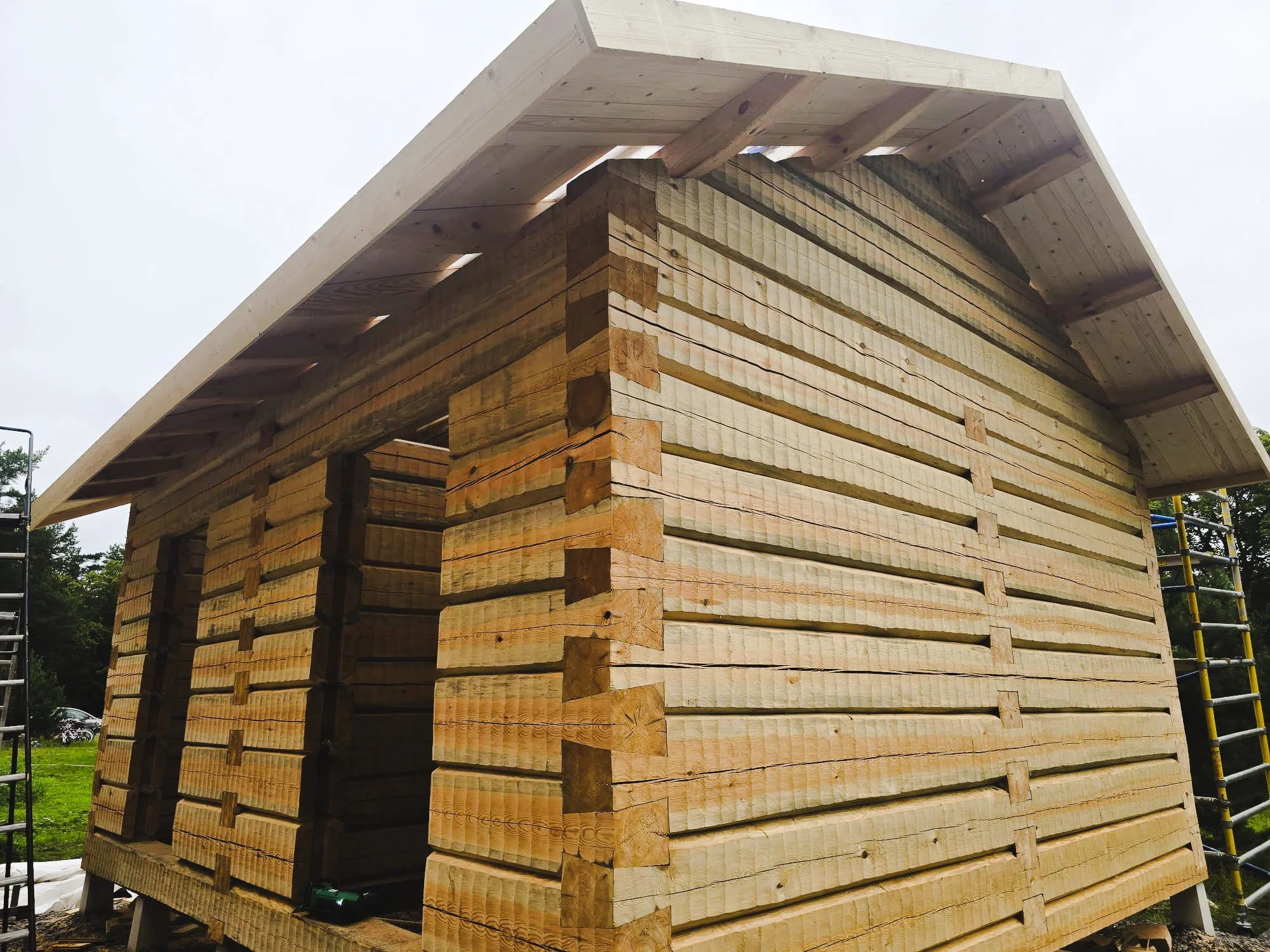 A wooden house under construction with horizontal wooden planks and a large overhanging roof.