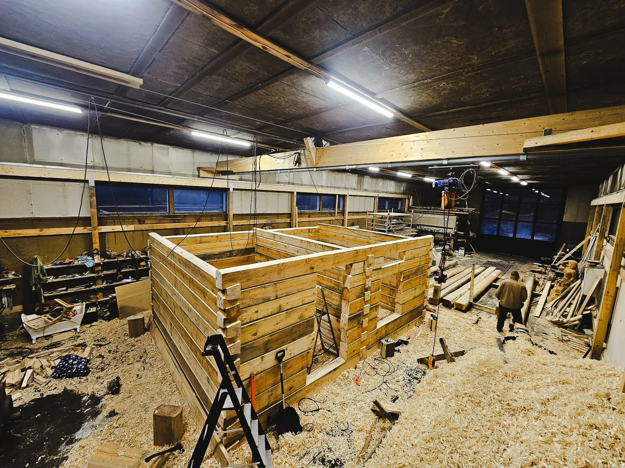 Interior of a building under construction with wooden framing, construction tools, and a person working on the site.