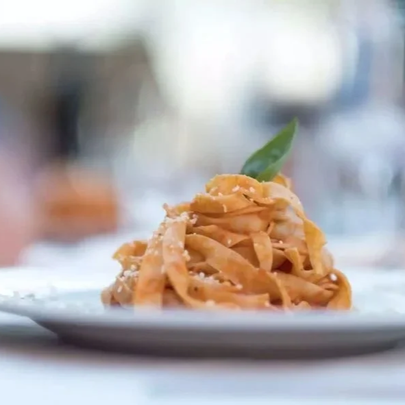 En tallerken med pasta garnert med en basilikablad, plassert på et bord med en utendørsbakgrunn.
