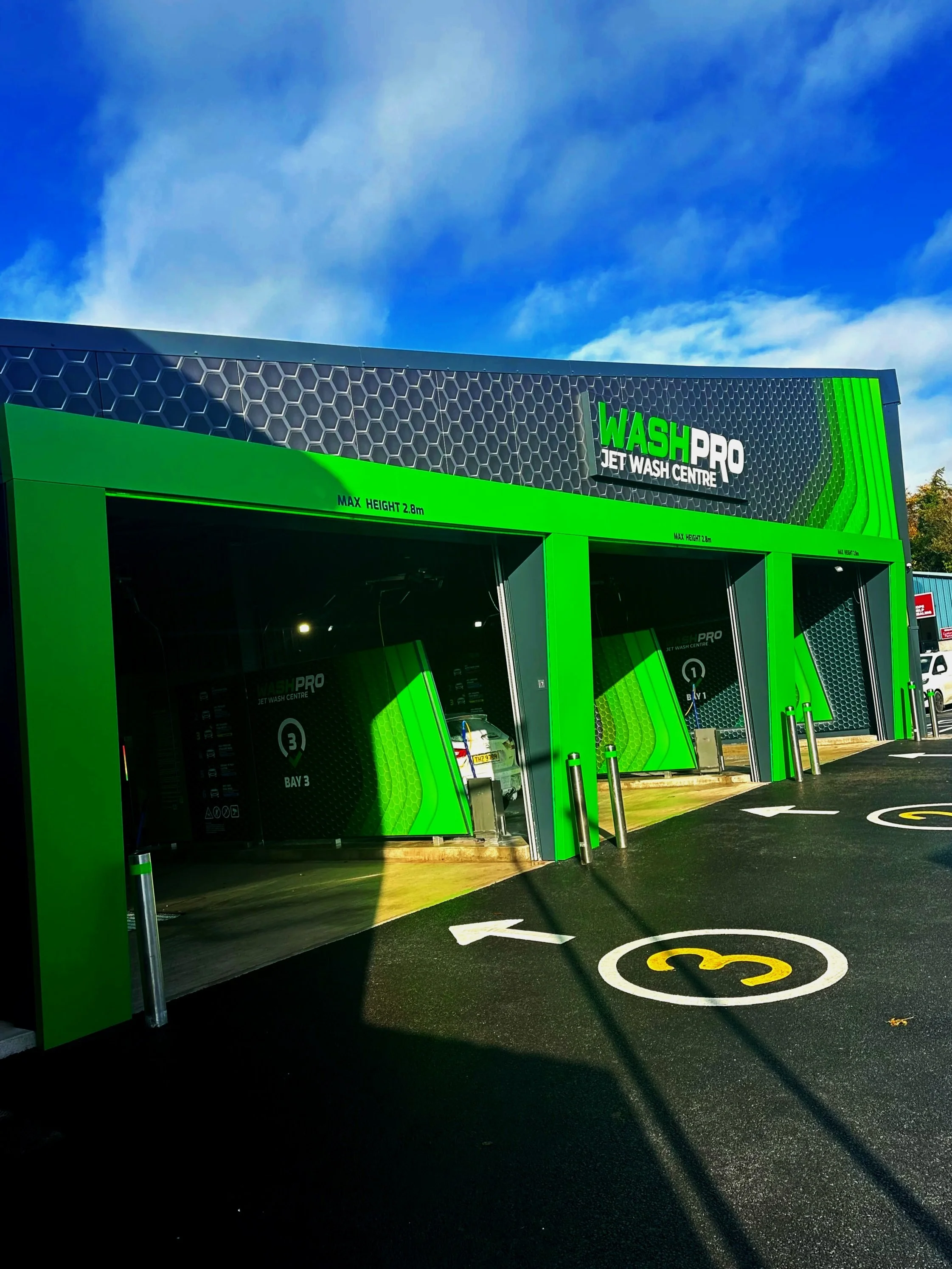Green and black jet wash center with three bays, marked with numbers 1, 2, and 3, under a blue sky with some clouds.