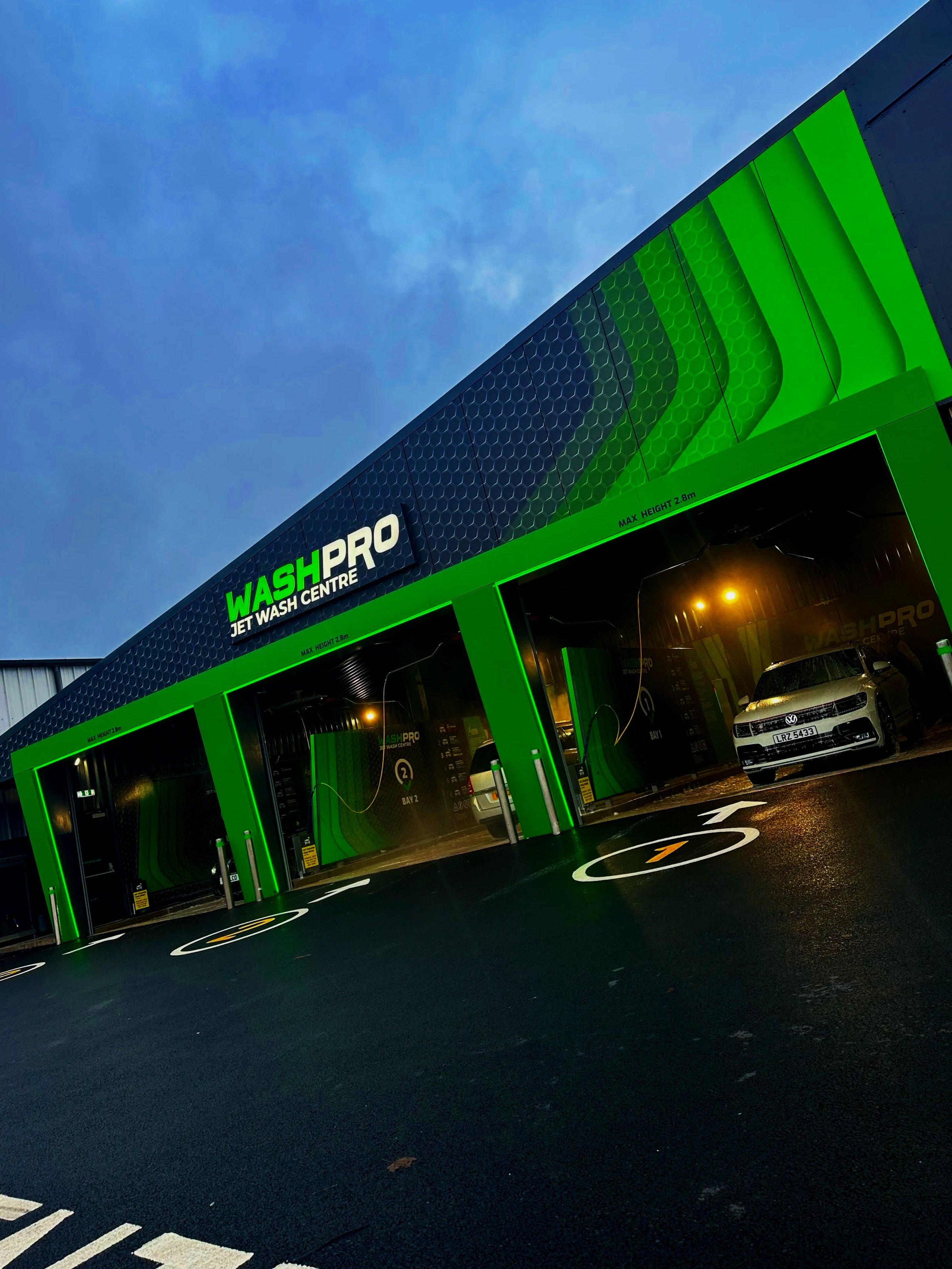 Exterior view of WashPro jet wash center with green and black design, cars inside washing bays, and parking spots in front.