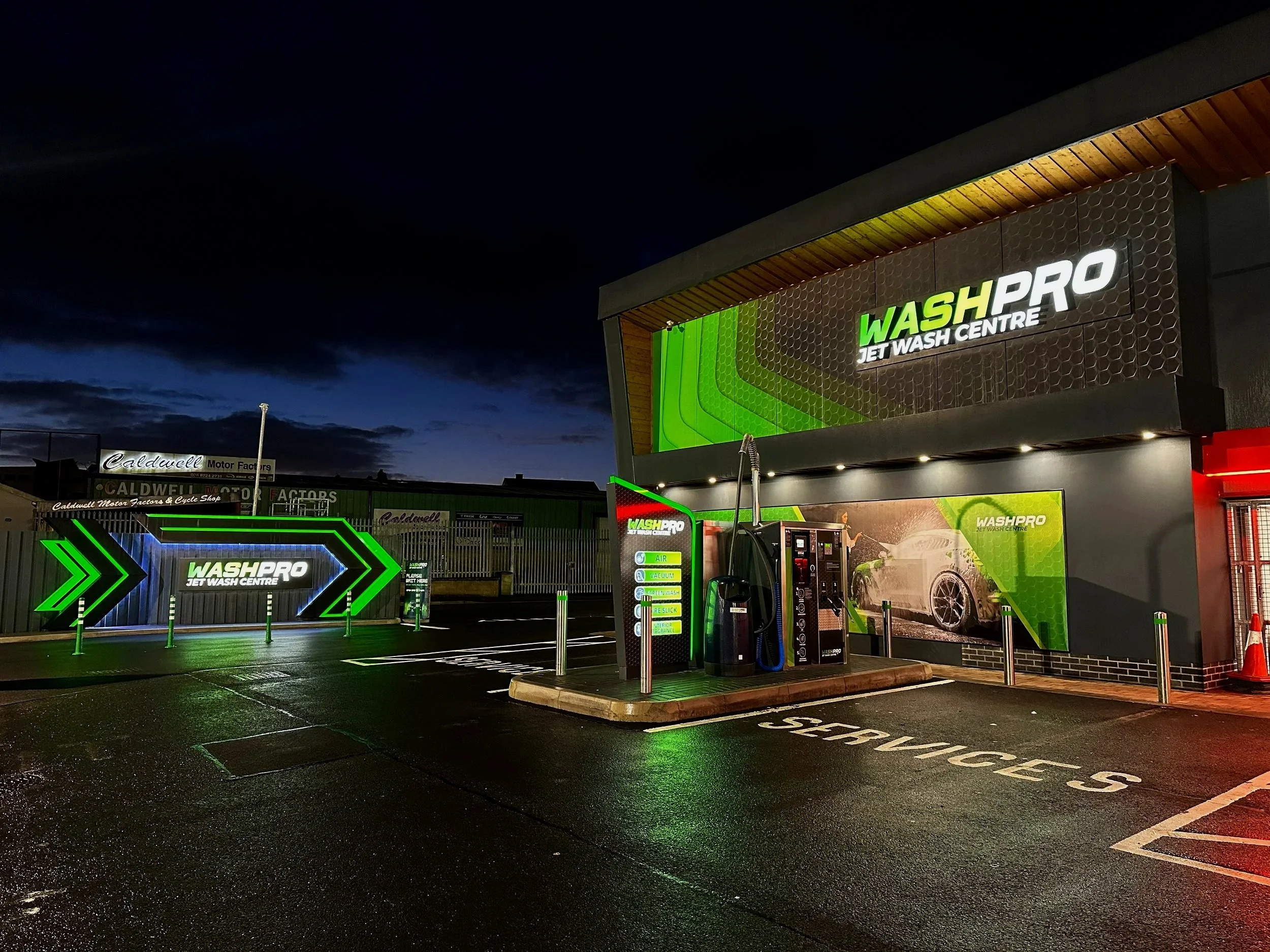 Nighttime exterior view of Wash Pro Jet Wash Centre with illuminated signs and parking area.