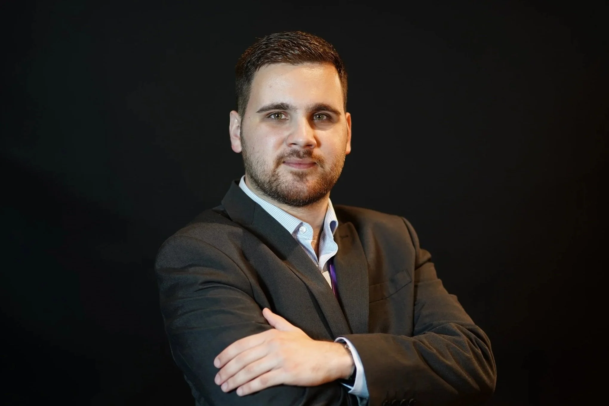 A portrait of director Balint Brunner posing in a dark business suit against a black background.