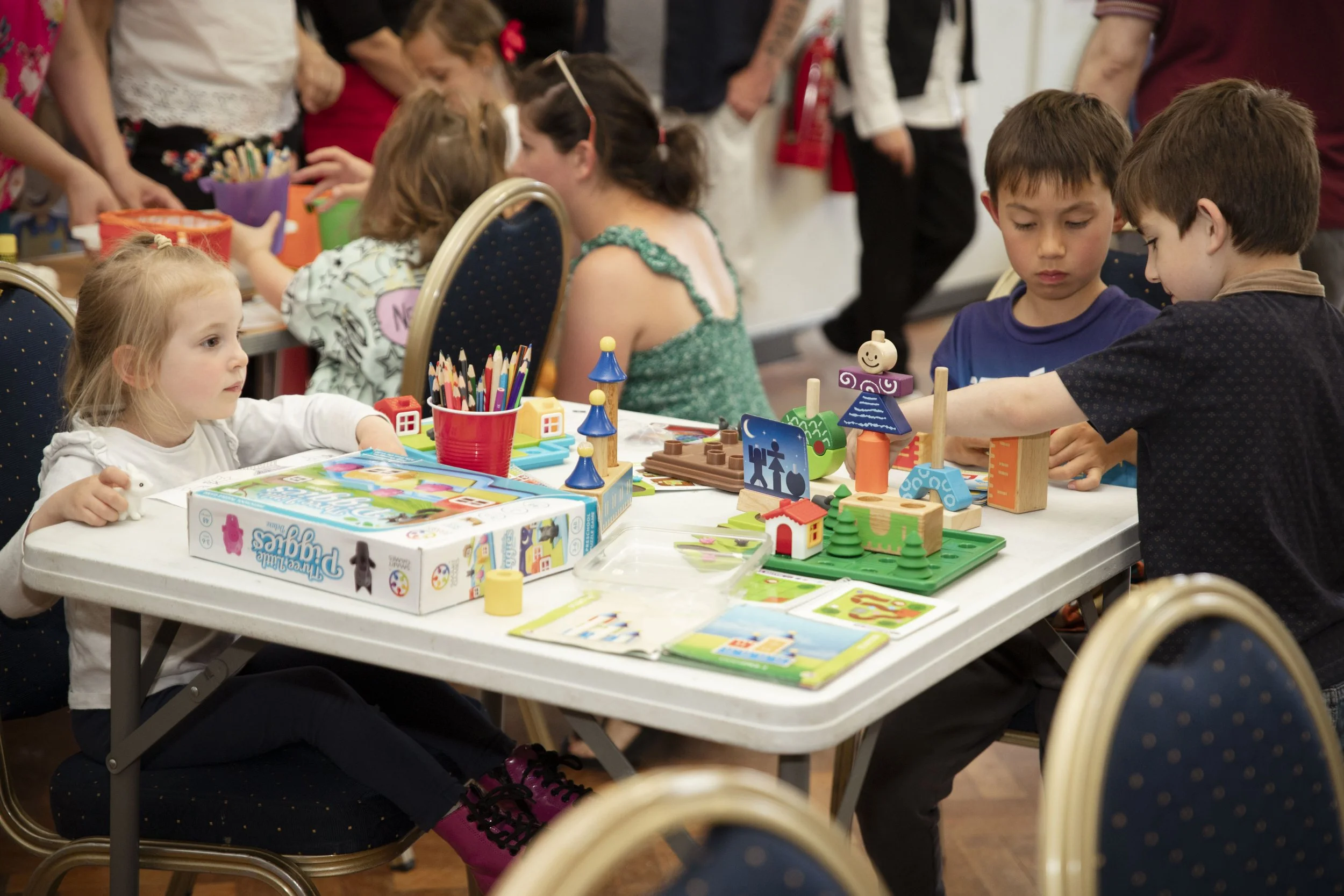 Children playing with colourful toys and building blocks on a table at a Welsh-Hungarian cultural event.