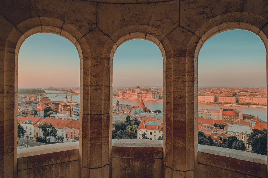 The view from among the pillars of Fisherman's Bastion in Budapest, featuring the River Danube and the Parliament of Hungary in the middle of the photo.