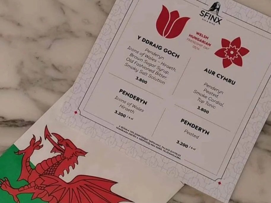 A photo of a special, limited edition drinks menu from Sfinx Gin & Wine Bar in Budapest featuring two Welsh-inspired cocktails with Penderyn whiskey, accompanied by a Welsh flag.