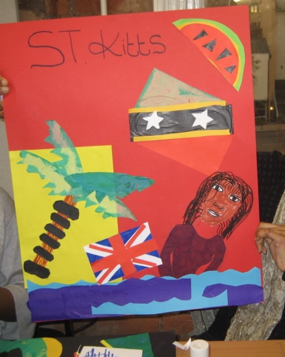A colorful poster with various drawings and cutouts, including a face, a rainbow, a British flag, and a dragon, with the text "St. Kitts" written at the top.