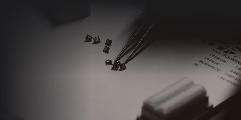 Jeweler's workspace with small gemstones being set with tweezers on a piece of paper, alongside a receipt and a rolled-up paper or cloth.