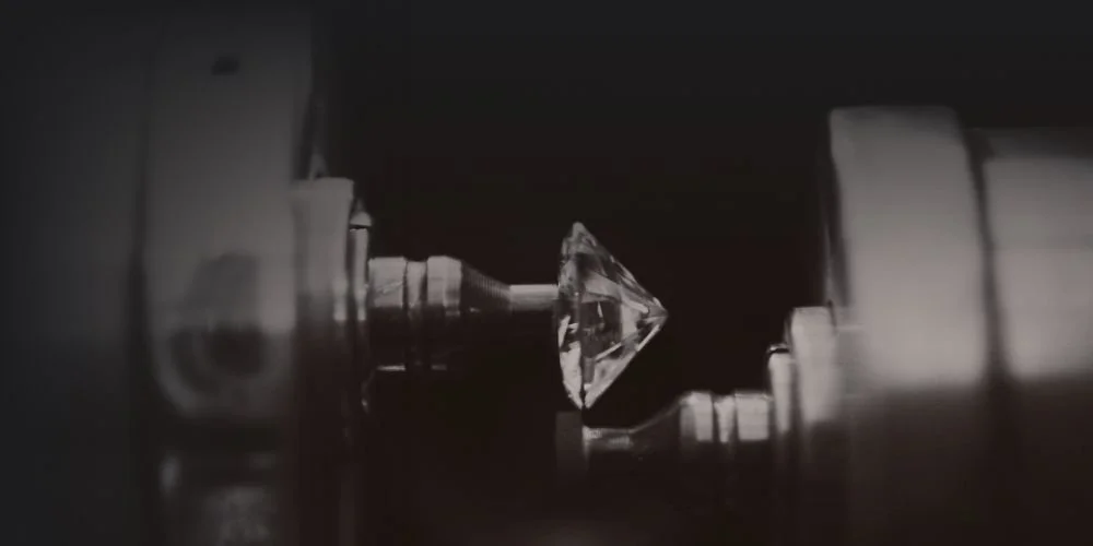 Close-up of a diamond-shaped gemstone set between two metallic components in a dark setting.