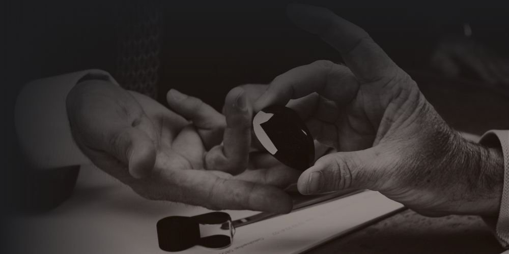 Close-up of an elderly person’s hands holding a black computer mouse, resting on a desk with a mouse pad.