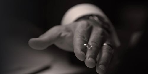 Close-up of a person's hand with rings on the fingers, extended forward, with a blurred background.