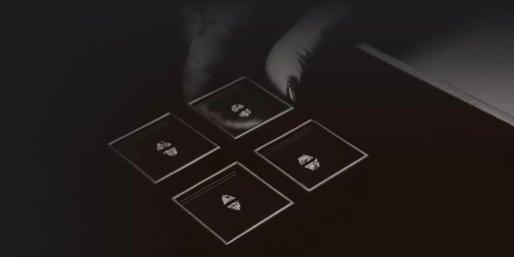 A person's hand selecting a black diamond ring from four black boxes on a dark surface.