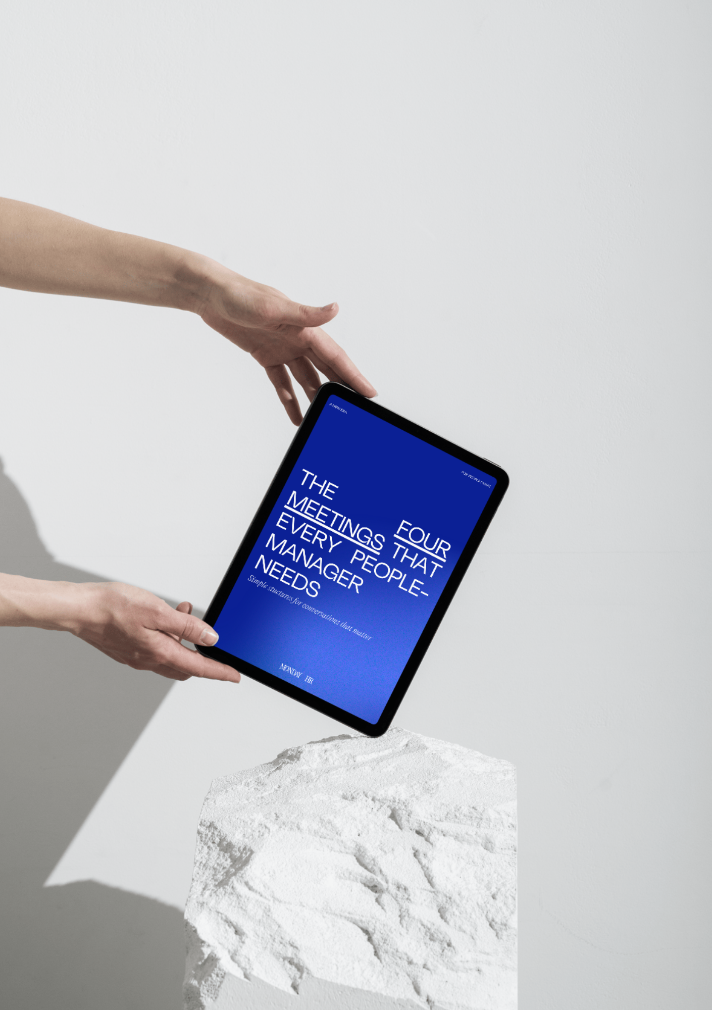 Person holding a tablet displaying a blue cover with white text that reads 'Four meetings that every people manager needs' and a subtitle 'Simple structured conversations that matter.' The tablet is above a white textured surface against a plain light background.