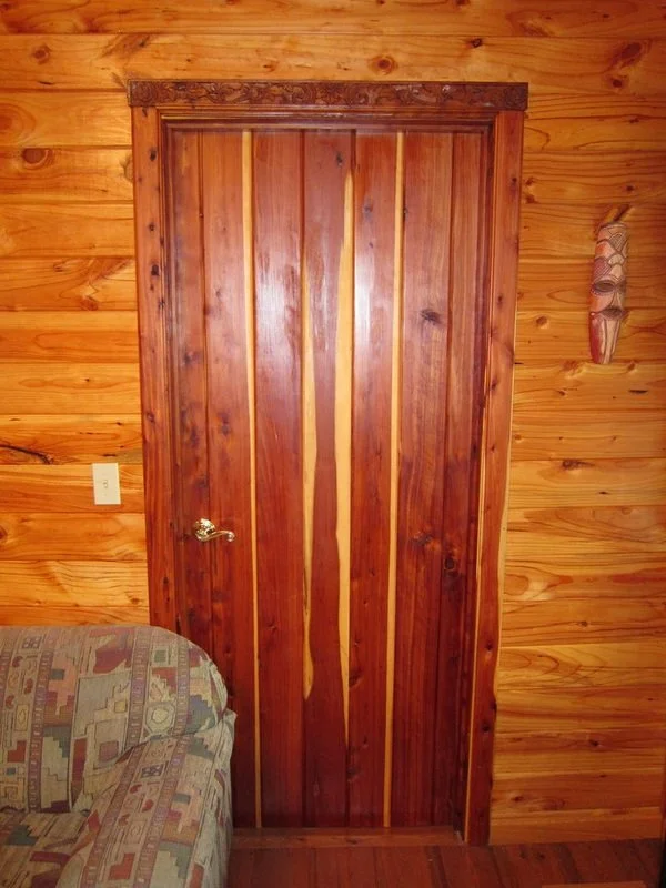 Wooden doorway with a vertically striped door set in wood-paneled wall, with a colorful patterned couch in front and wall decor to the right.