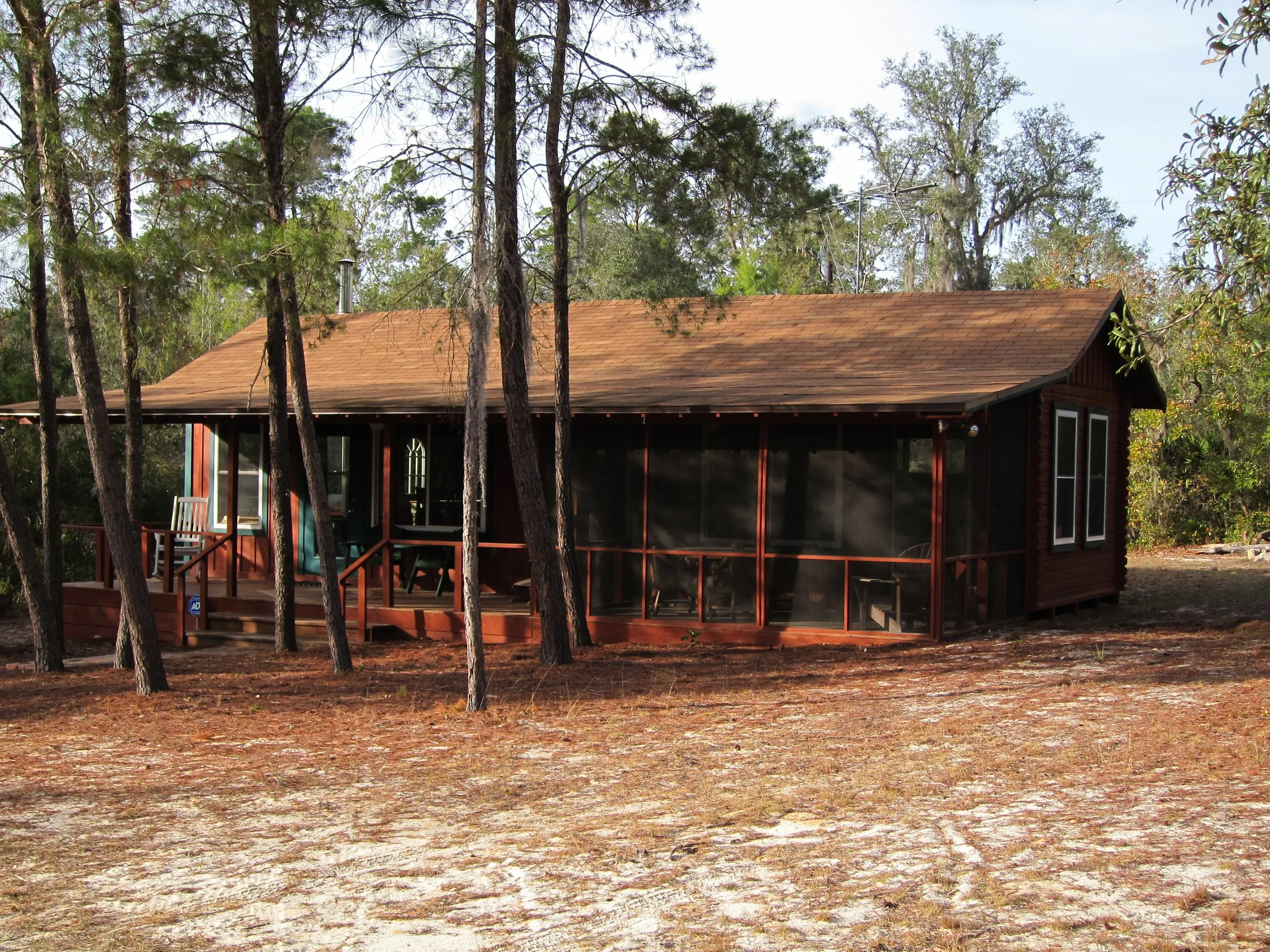 A house surrounded by trees with a front porch and screened-in porch area.