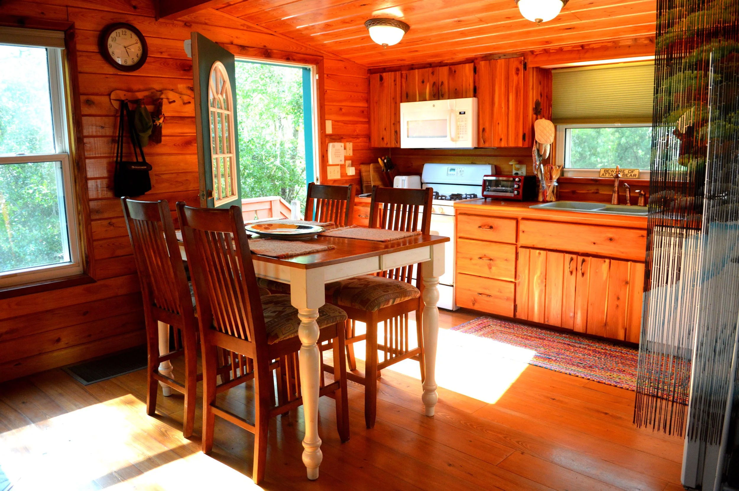 Wood-paneled cabin kitchen with wooden dining table and chairs, window, door leading outdoors, stove, microwave, and small countertop appliances.