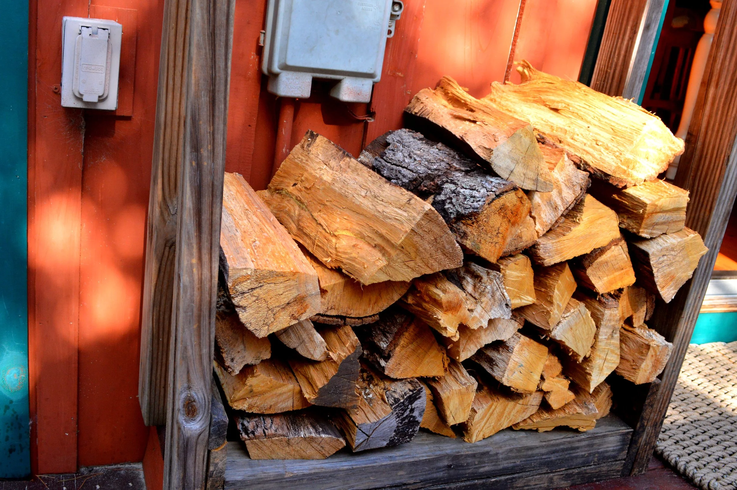 A stack of firewood logs neatly arranged on a wooden rack against an orange wall.