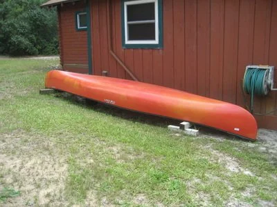 An orange kayak resting on supports outside a red house with a window and a garden hose reel.