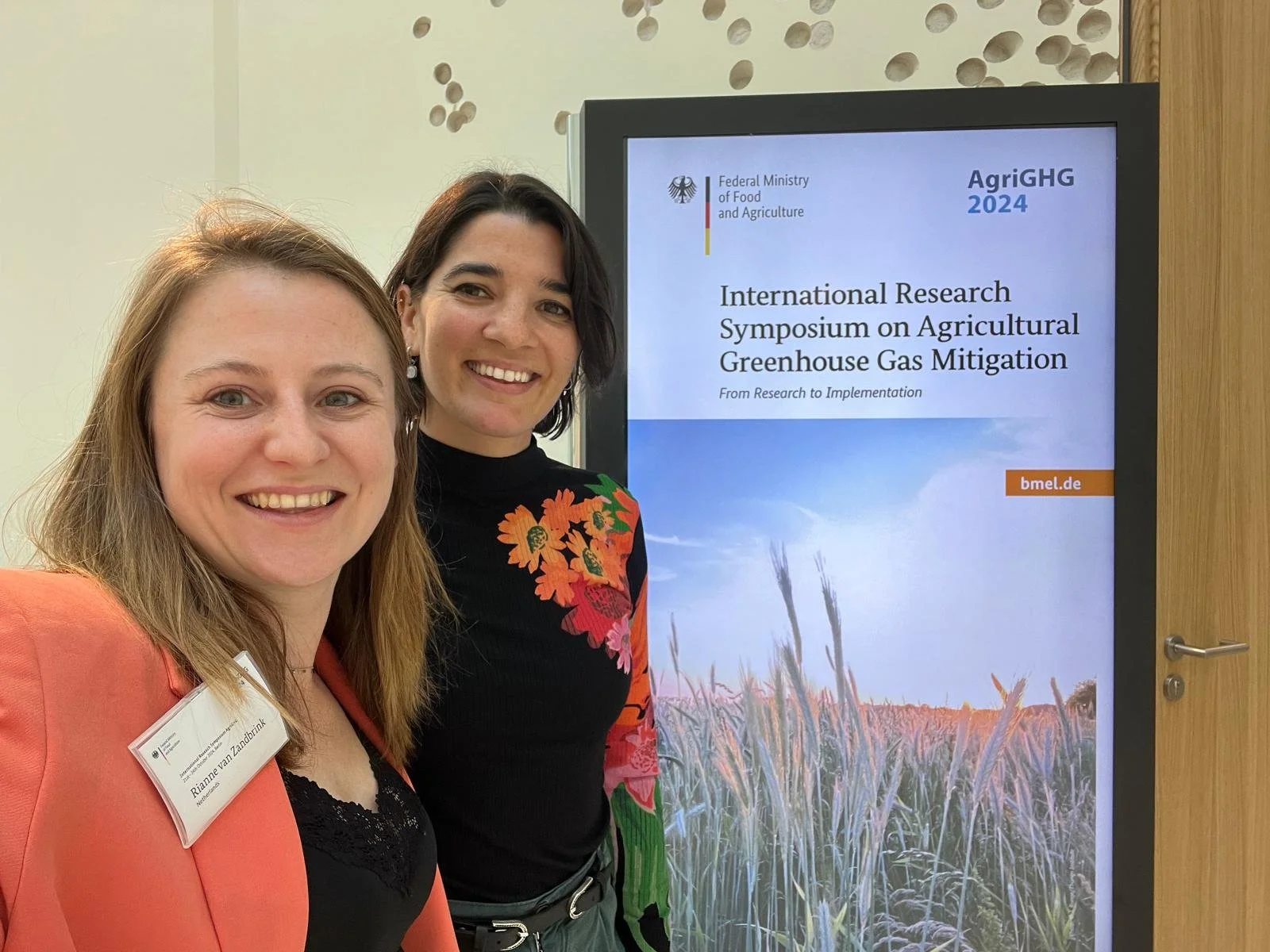 Co-leads of the CFS network, standing next to a digital display showing information about the International Research Symposium on Agricultural Greenhouse Gas Mitigation, organized by the German Federal Ministry of Food and Agriculture in 2024.