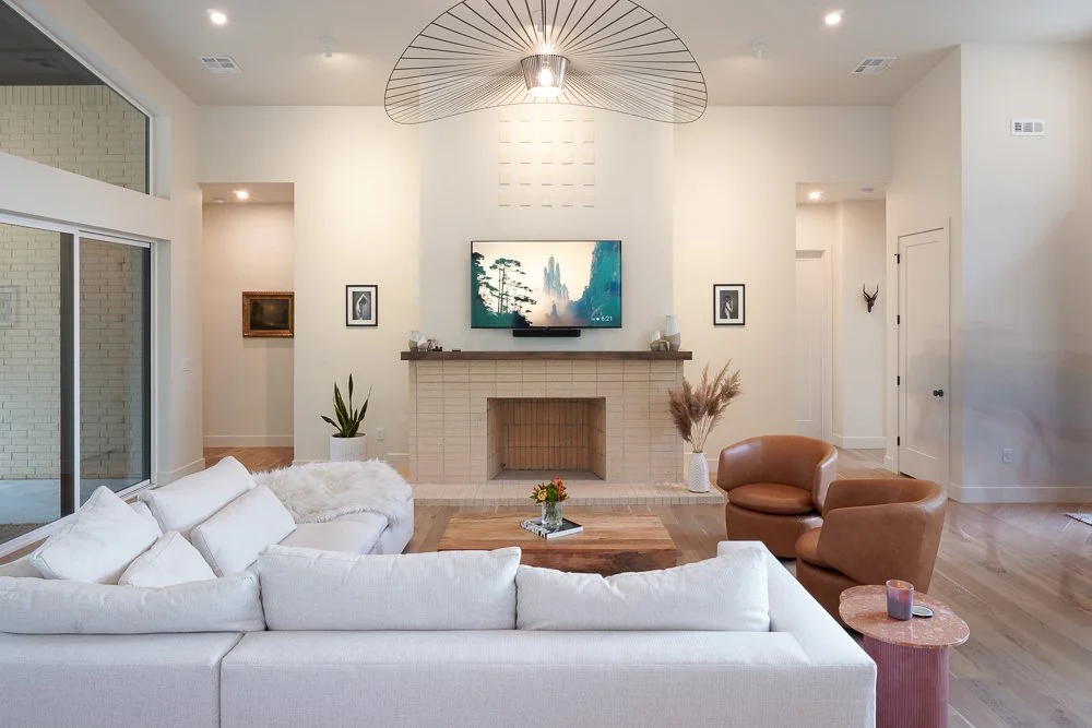 Modern living room with white sofa, brown armchairs, fireplace, wall-mounted TV, and decorative plants.
