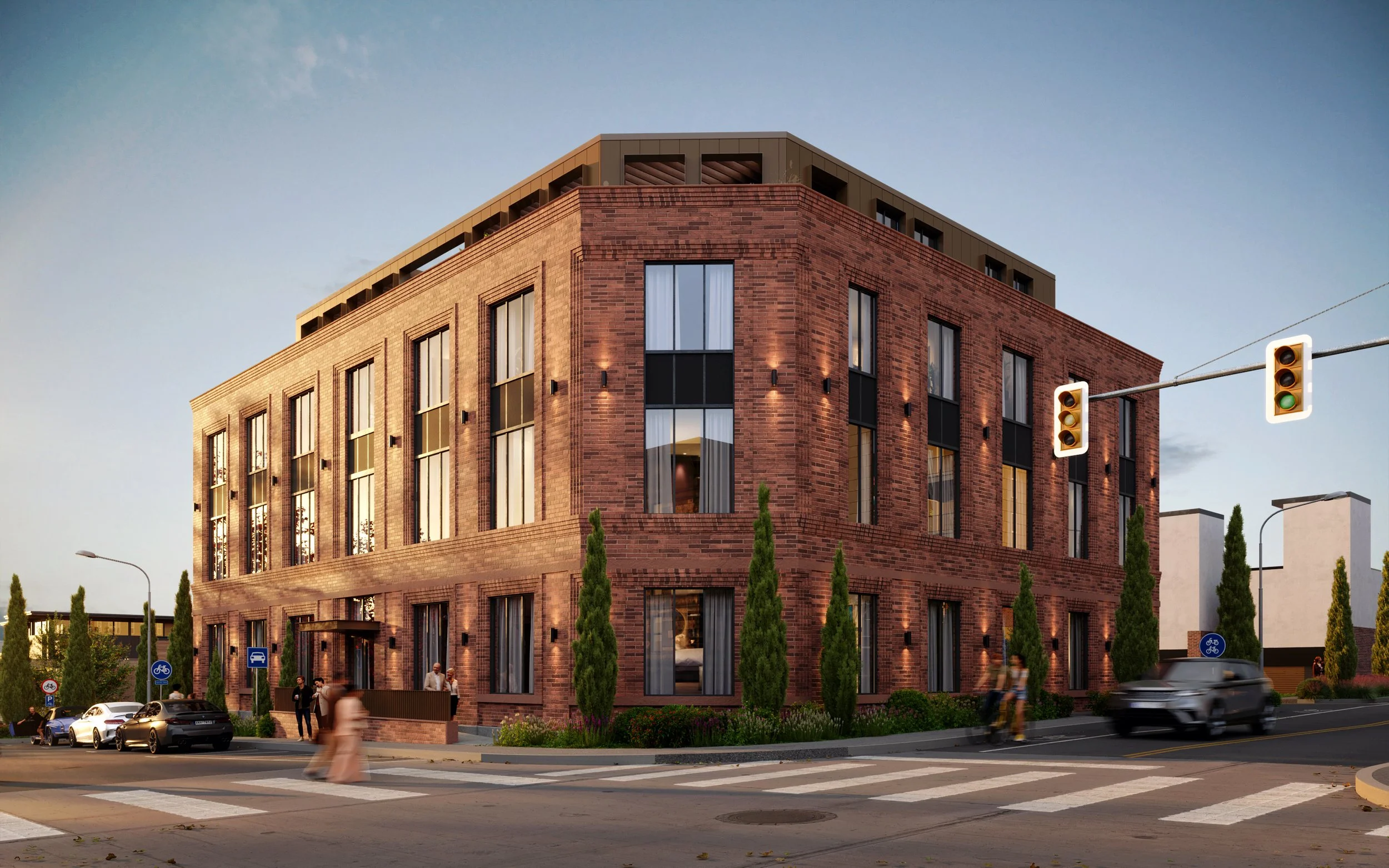 A modern, multi-story brick building on a city corner, with tall windows, street trees, cars, bicycles, and pedestrians crossing at a zebra crosswalk during dusk.
