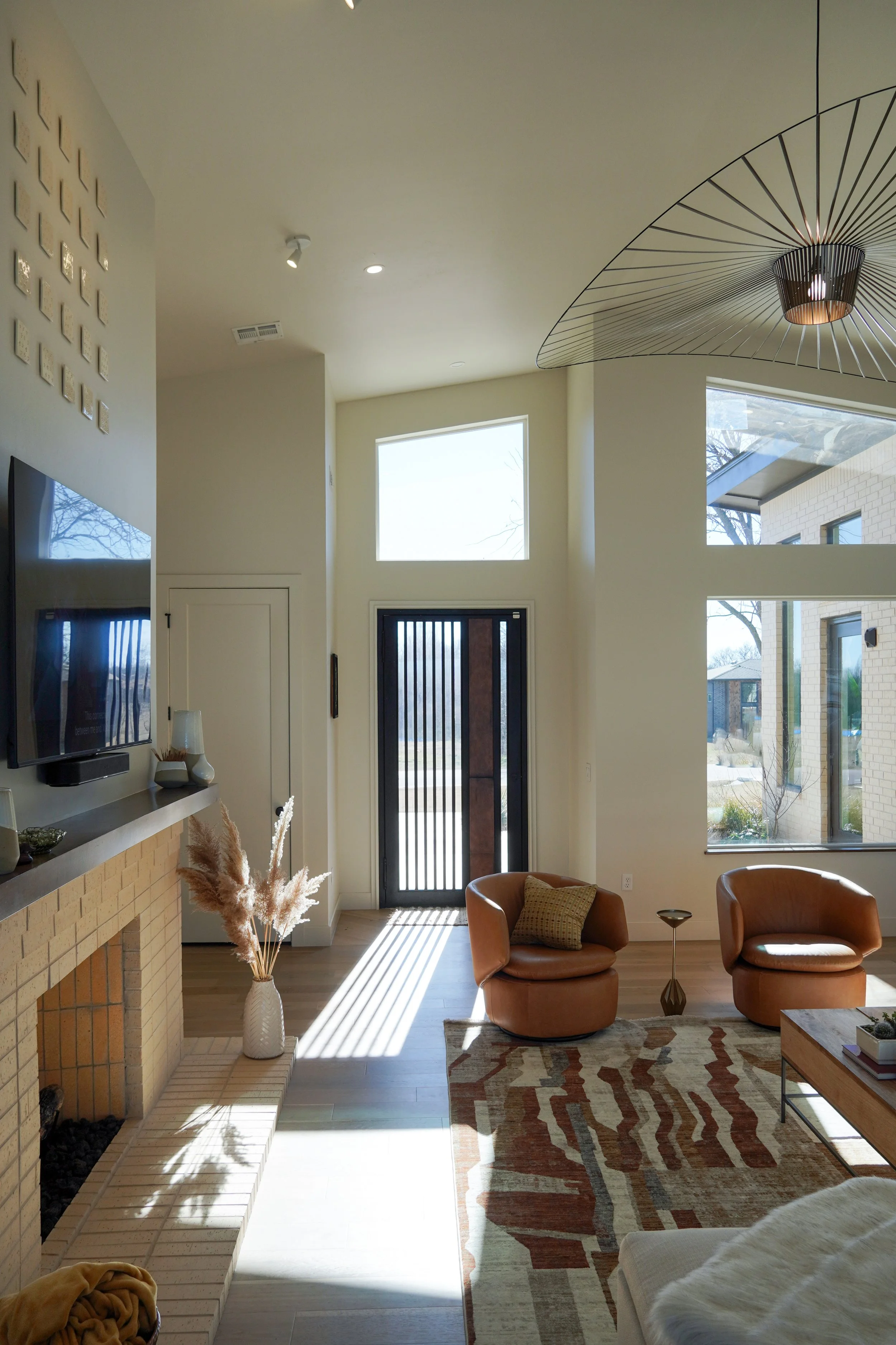 Bright modern living room with large windows, a fireplace, and leather chairs, illuminated by natural light.