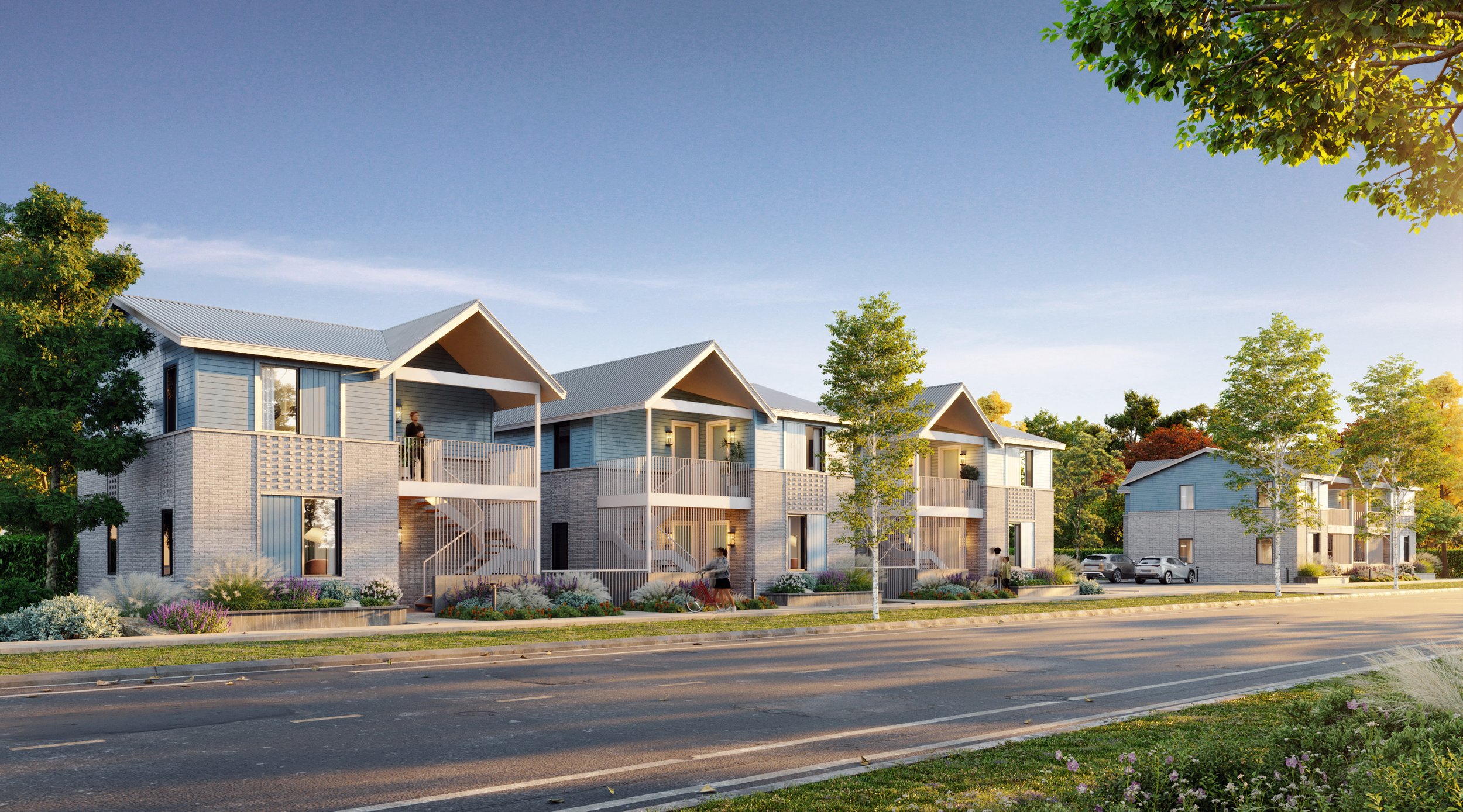 Modern residential townhouses with light blue siding and gray roofs, trees and landscaped gardens, cars parked, and people walking and standing outside.