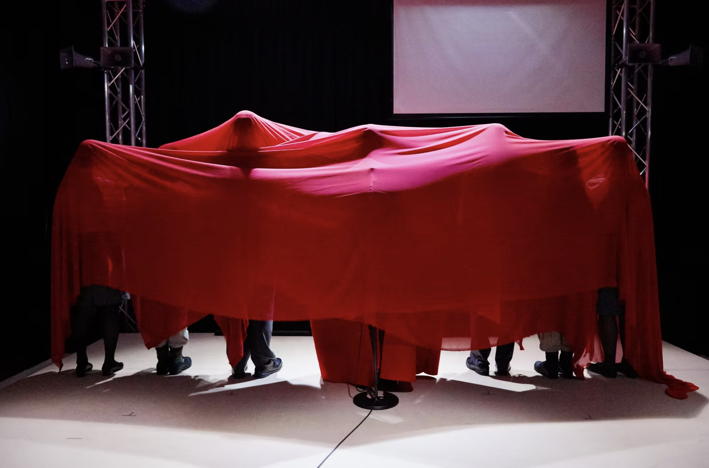 People on stage unveiling a car covered with a red cloth at an event or presentation.