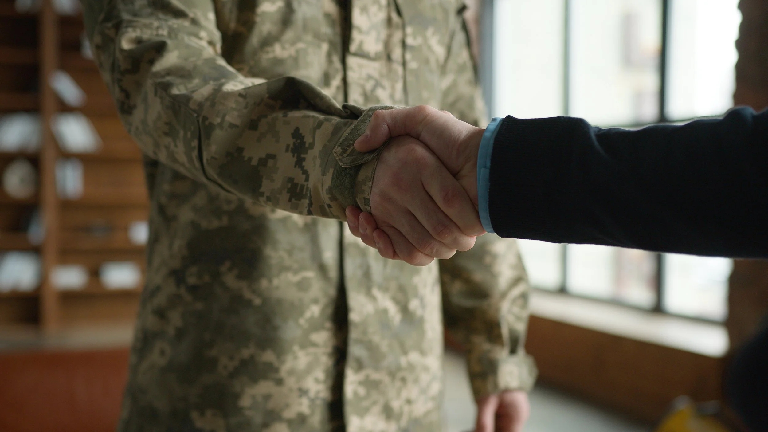 Two individuals shaking hands, one in military camouflage uniform.