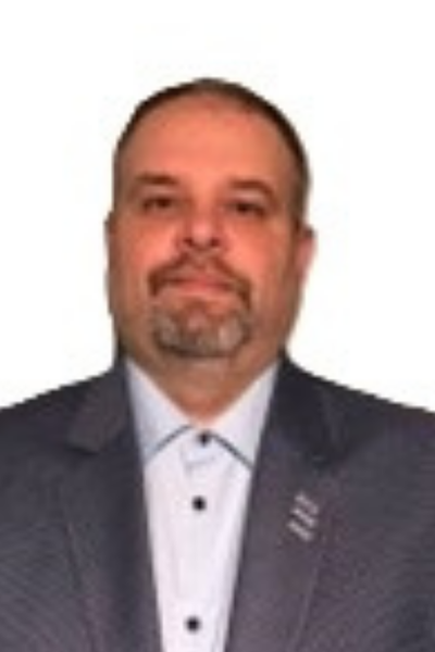 A man with short hair, a beard, and mustache wearing a suit jacket and a white dress shirt, posing for a portrait against a white background.