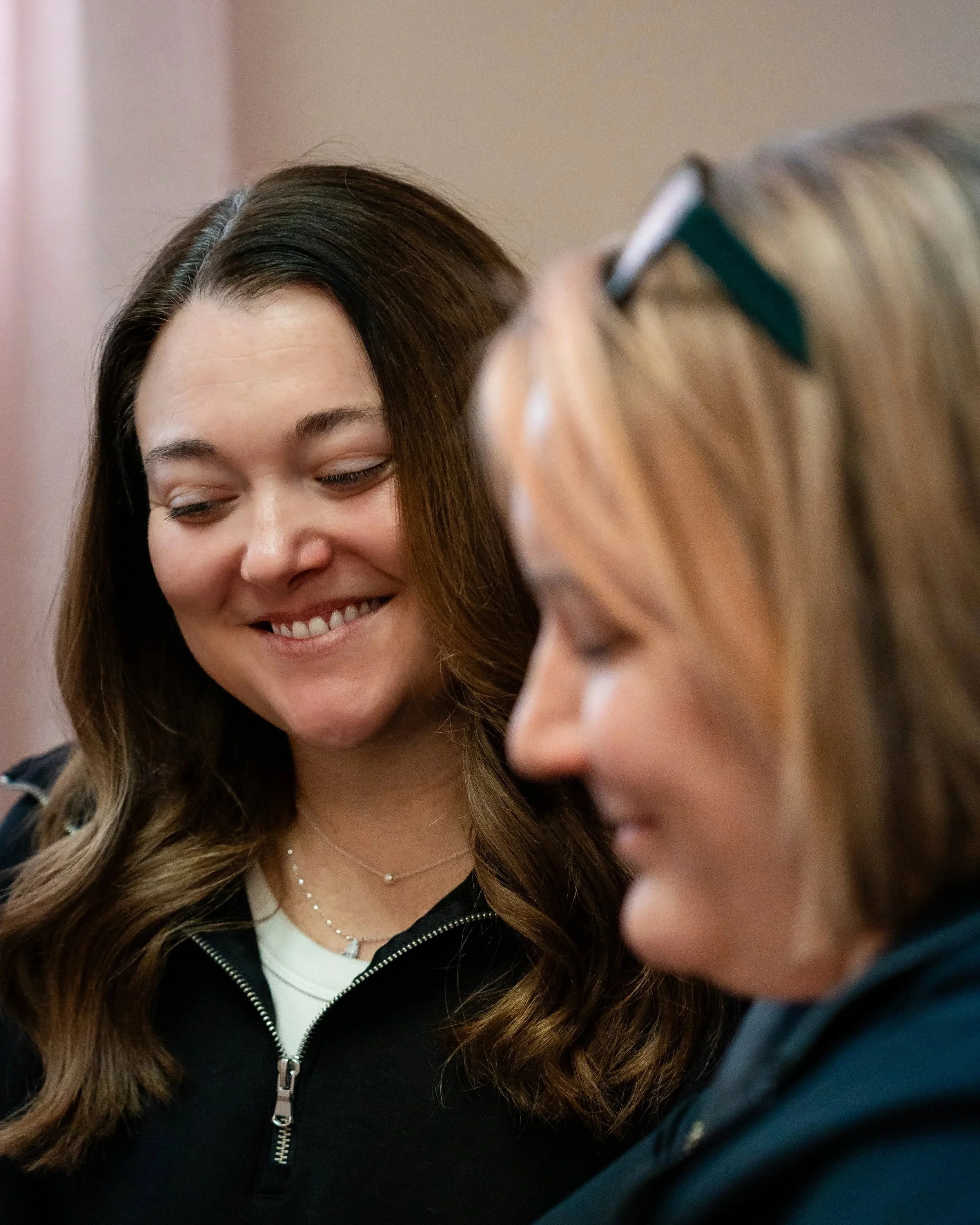 The Owner of Willow Skin Therapy in Cincinnati Consulting with a patient, two women smiling and close together, one with dark brown hair and the other with light reddish-brown hair and glasses.