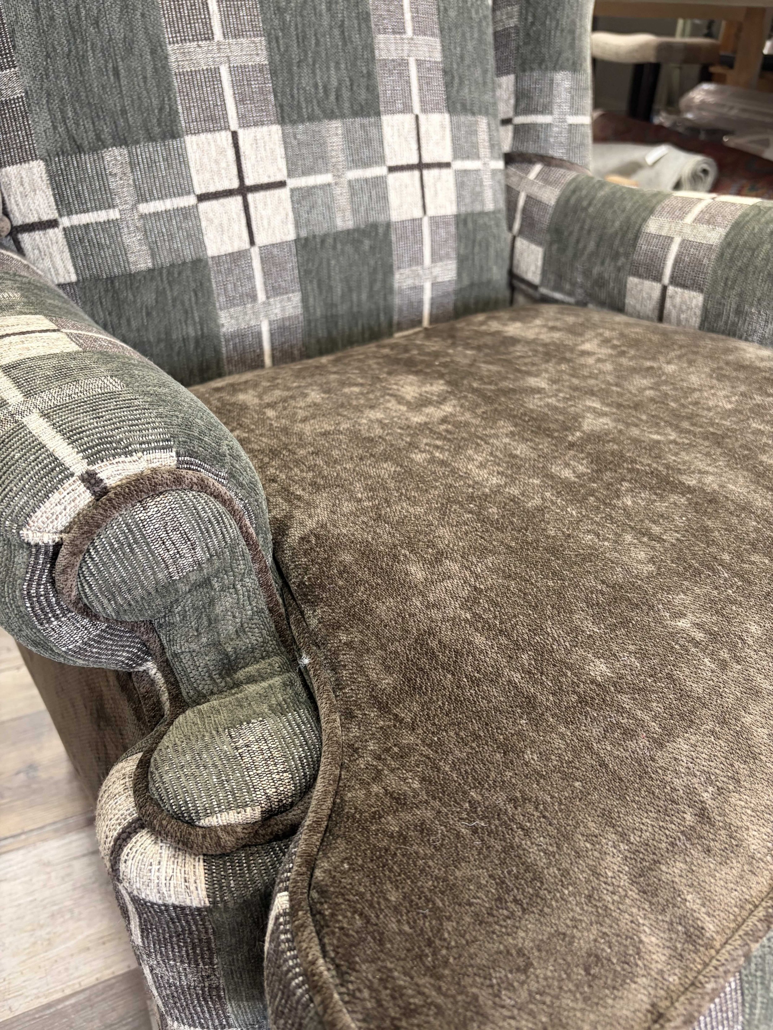 Close-up of a brown upholstered seat and checkered fabric armrest on a vintage-style armchair.