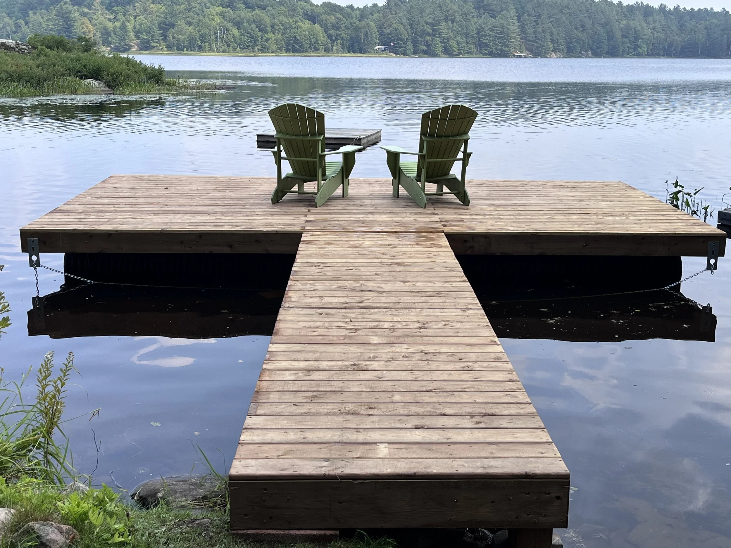 Two green Muskoka chairs on the end of a dock