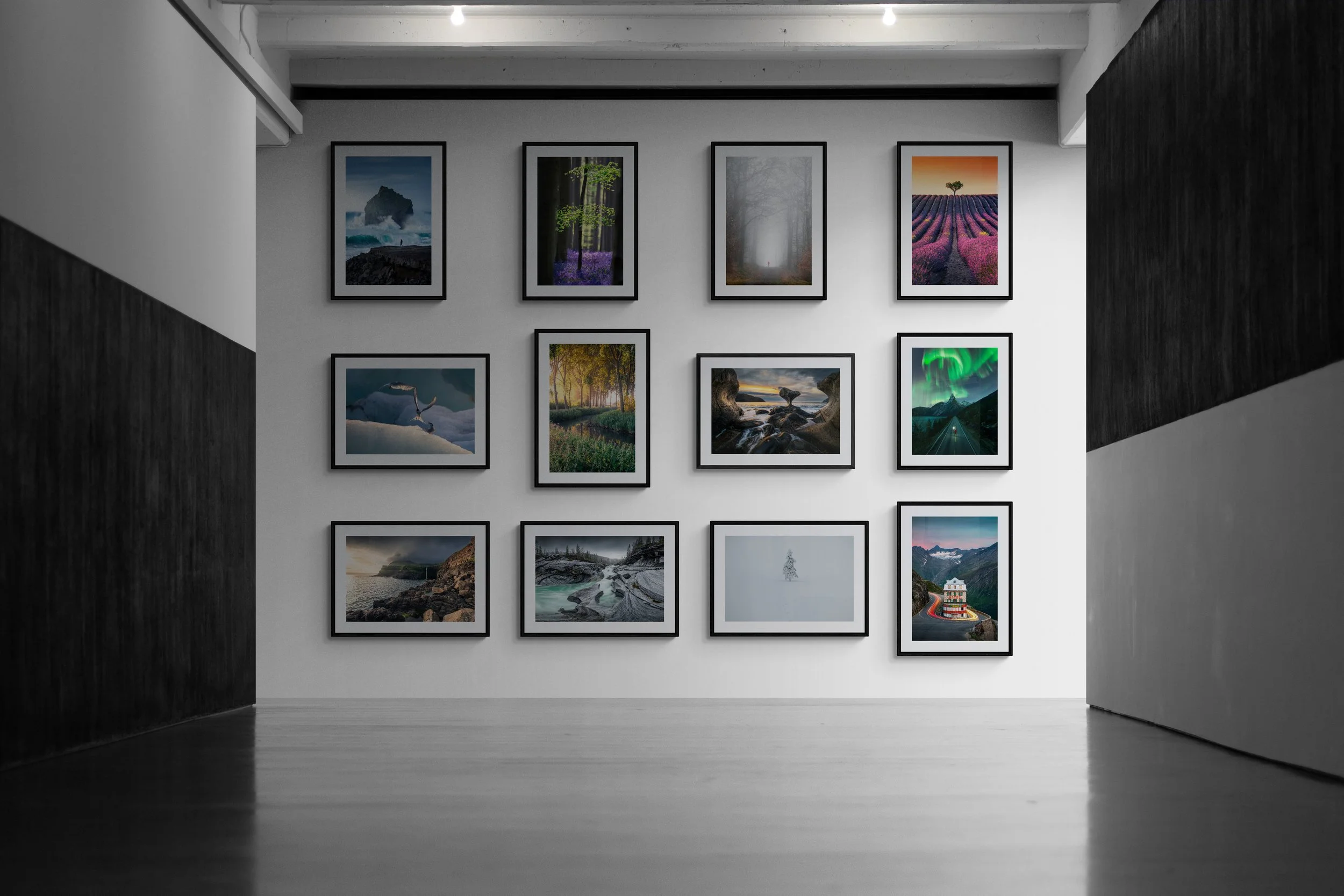 An art gallery with a white wall displaying twelve framed landscape photographs arranged in four rows. The photographs depict various natural scenery including mountains, forests, waterfalls, and lavender fields. The gallery has a minimalist design with a dark accent wall on the right and wood flooring.
