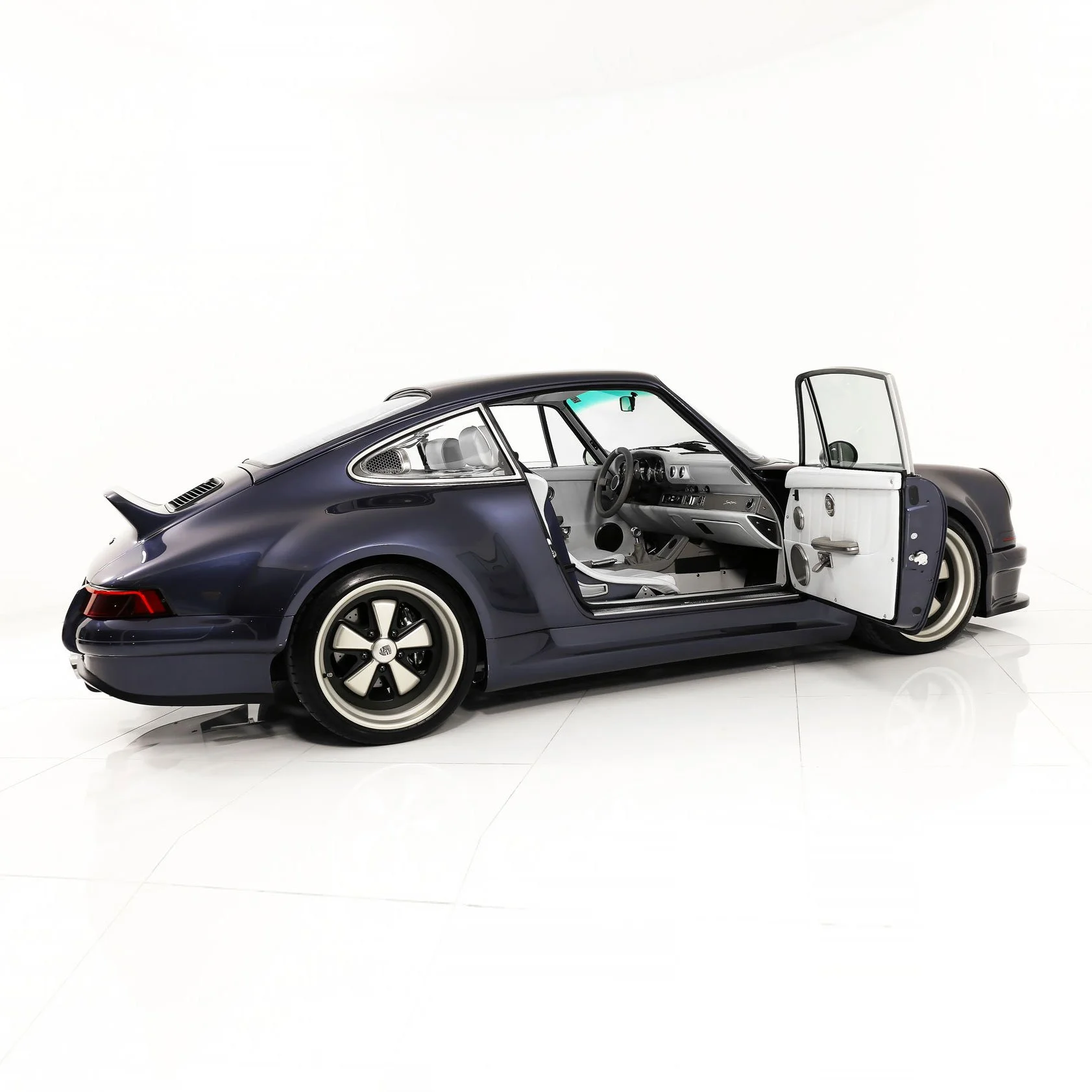 A classic dark blue sports car with a side door open, showing a white interior, against a plain white background.