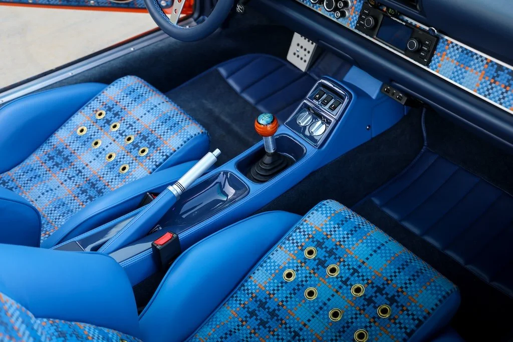 Interior of a classic car with blue seats and a plaid fabric pattern, manual gear shift, and dashboard controls.
