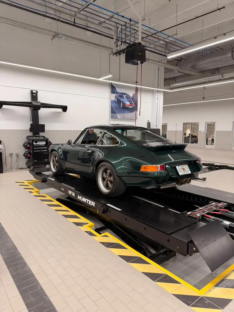 A green classic Porsche 911 sports car on a motion simulation platform in a showroom or testing facility.