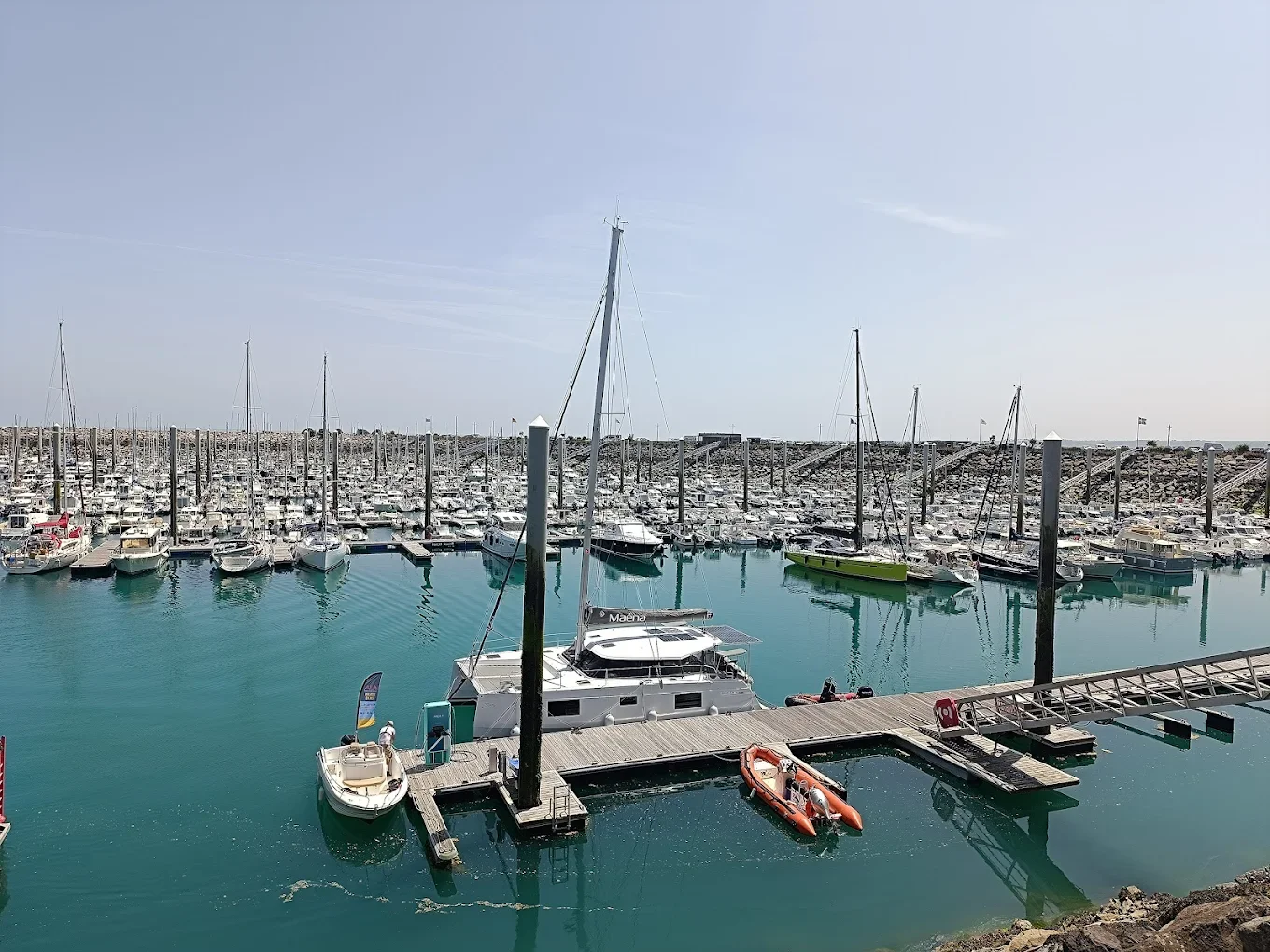 Port de plaisance avec de nombreux yachts amarrés, eaux calmes, ciel clair, vue panoramique.