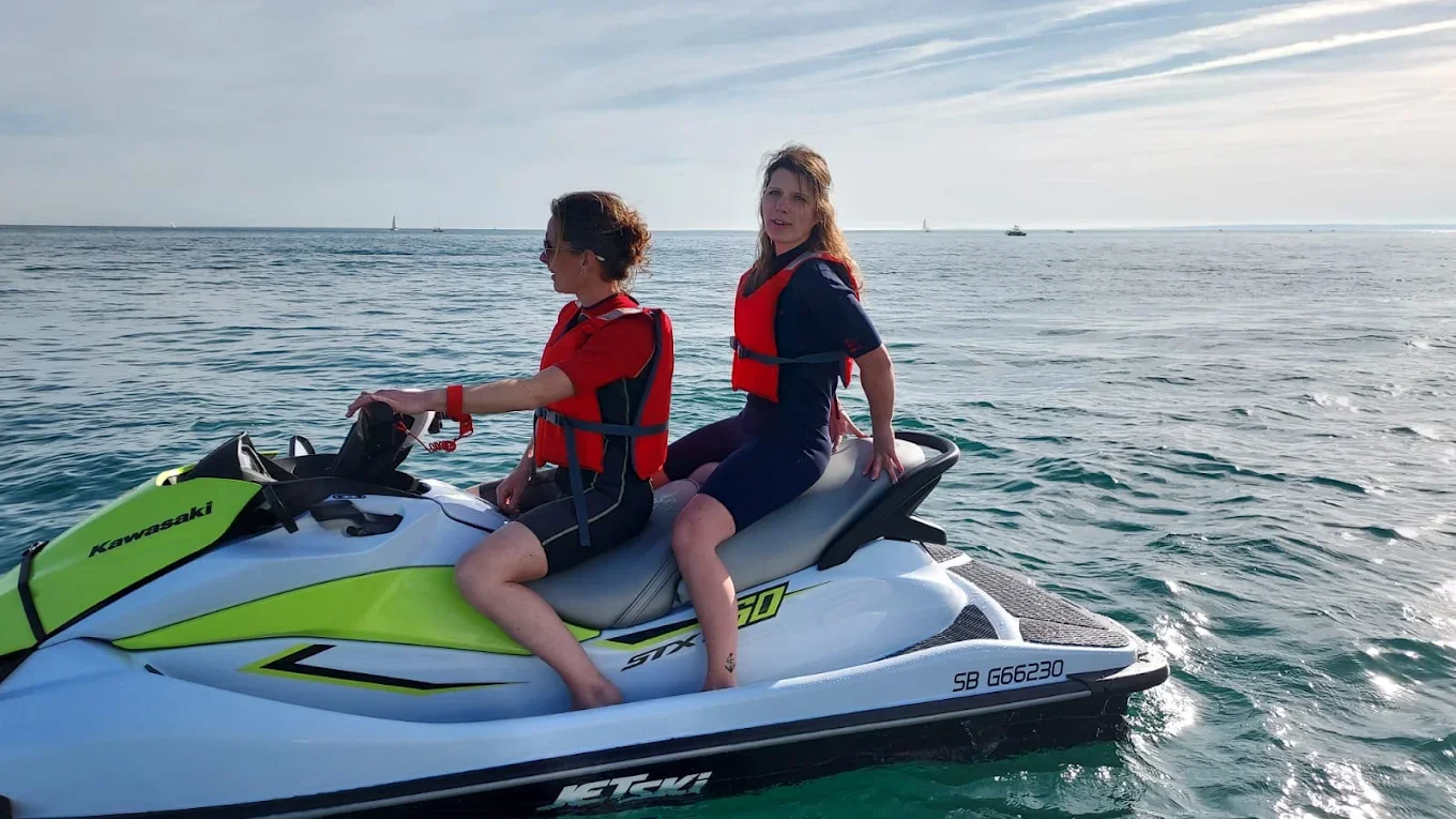Deux femmes sur un jet ski Kawasaki sur l'eau avec un ciel partiellement nuageux en arrière-plan.