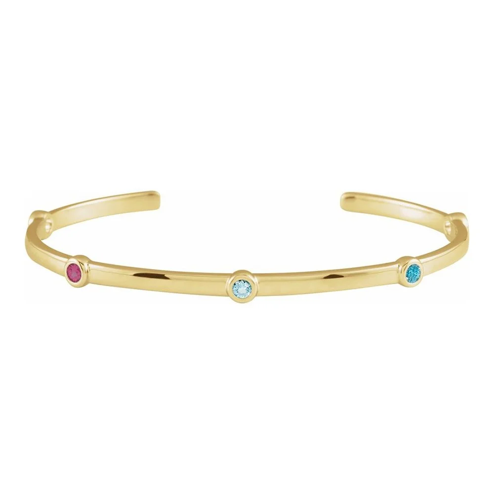 Gold open cuff bracelet with three small round gemstones in pink, blue, and turquoise.