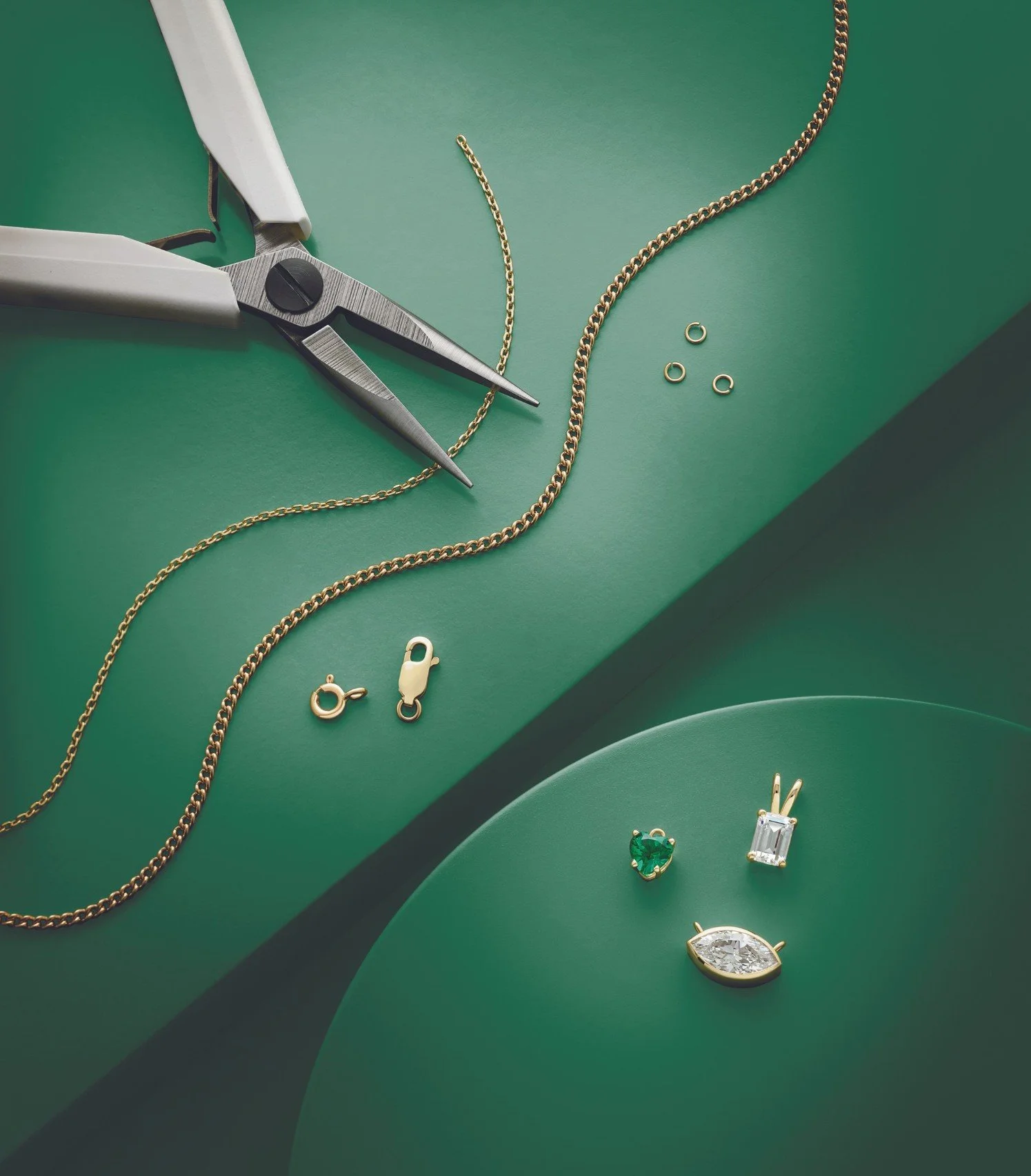 Jewelry making tools and various gold and gemstone pendants on a green surface