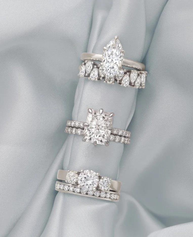 Three sparkling diamond rings with various designs resting on a light-colored fabric background.