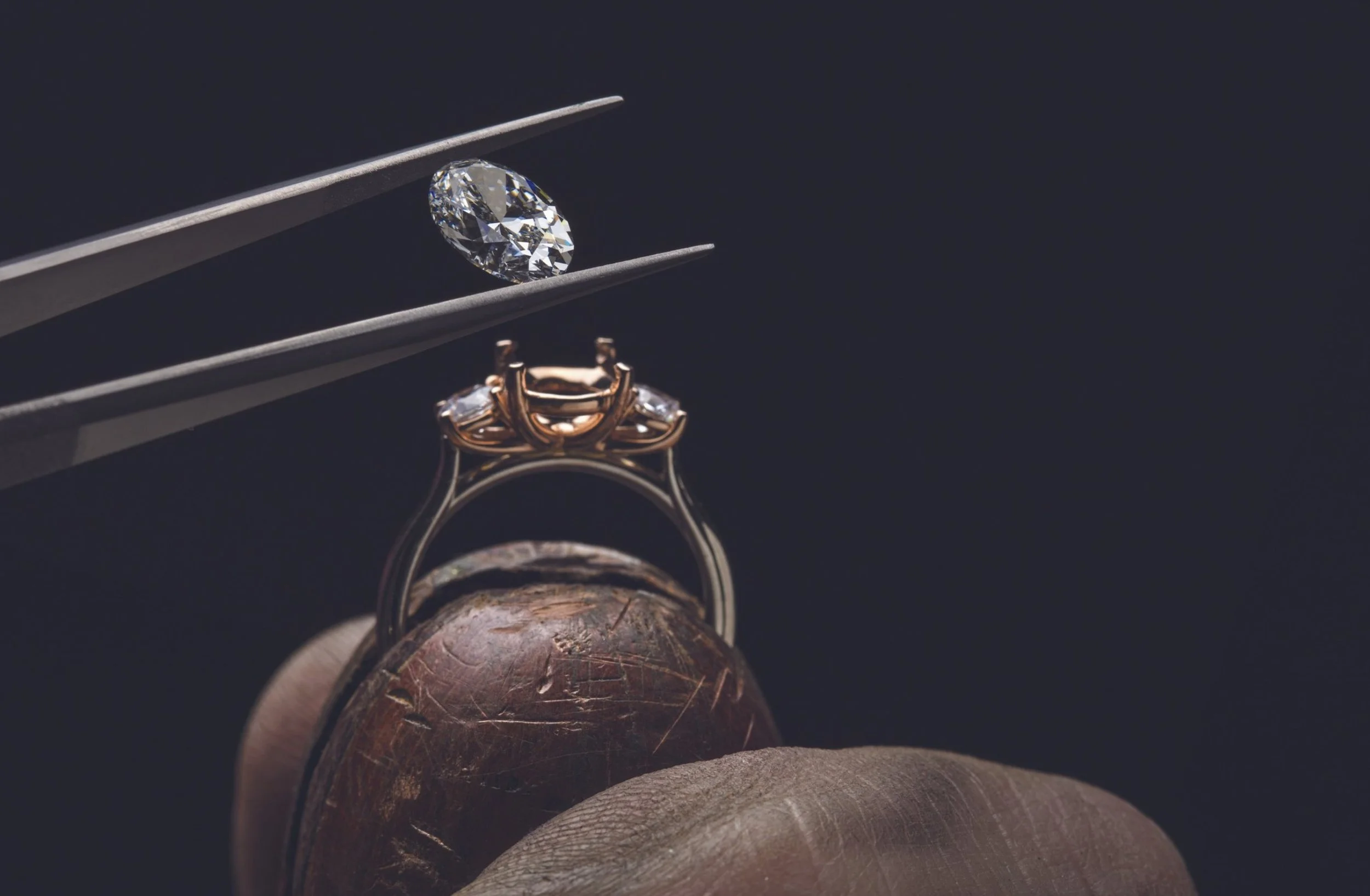 A diamond being held by tweezers above a ring, with a tester's block underneath.